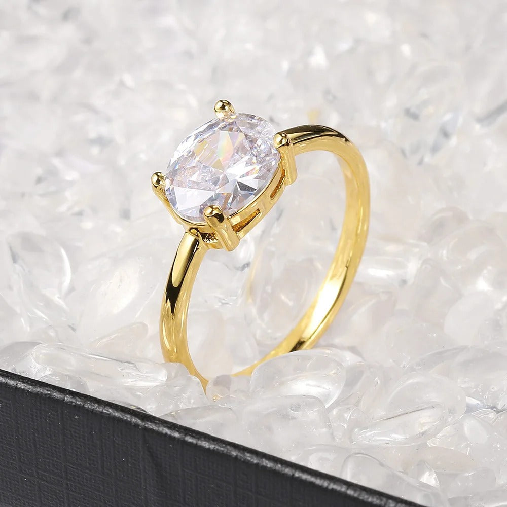 Anillo dorado brillante con piedra ovalada transparente y diseño sencillo